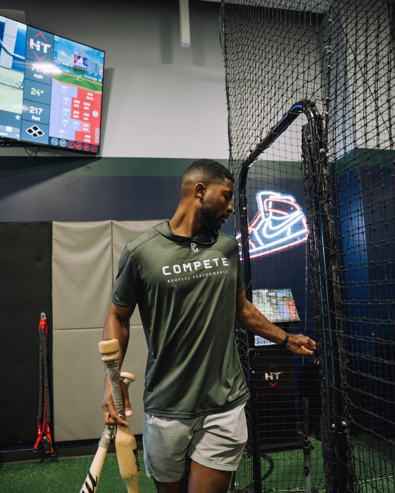 Compete BP hitting coach with bats beside the HitTrax screen