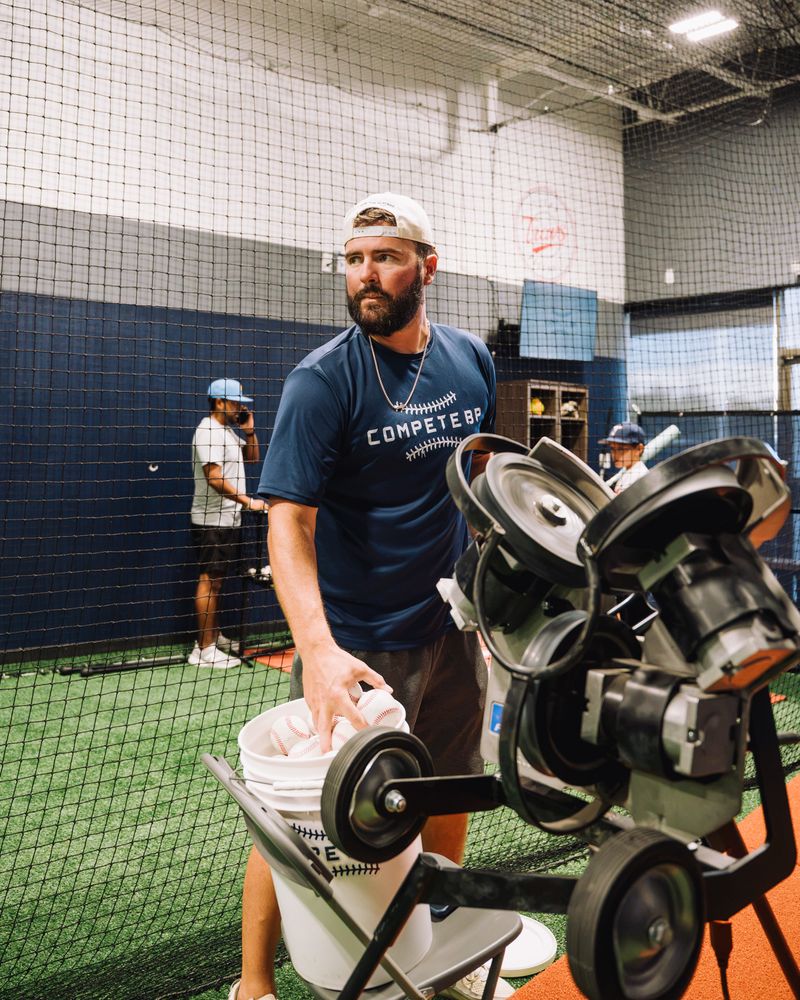 Compete BP coach loading a pitching machine in a batting cage