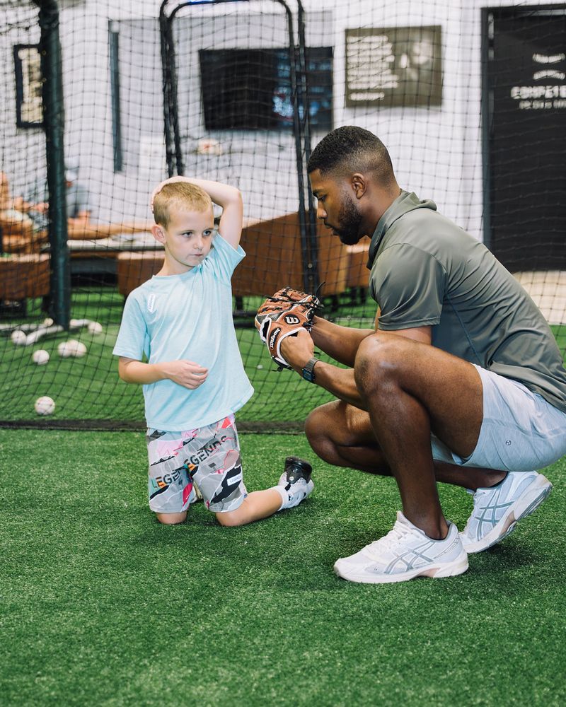 Compete BP coach kneeling beside a young player during a class