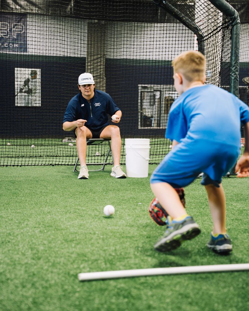 Young infielder fielding a ground ball while a coach watches